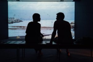 silhouettes of two people sat in a dark room against a bright screen