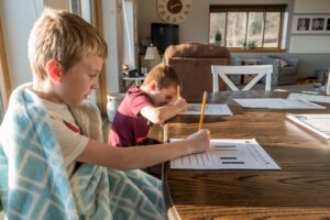 two boys writing on worksheets at a kitchen table
