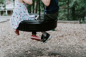 a litttle girl and boy sat on a tyre swing