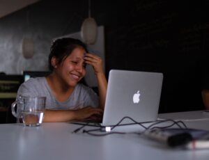 a woman smiling while she uses a laptop at a table