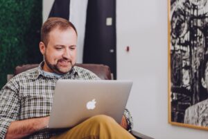 a white man with a beard uses a laptop balanced on his leg