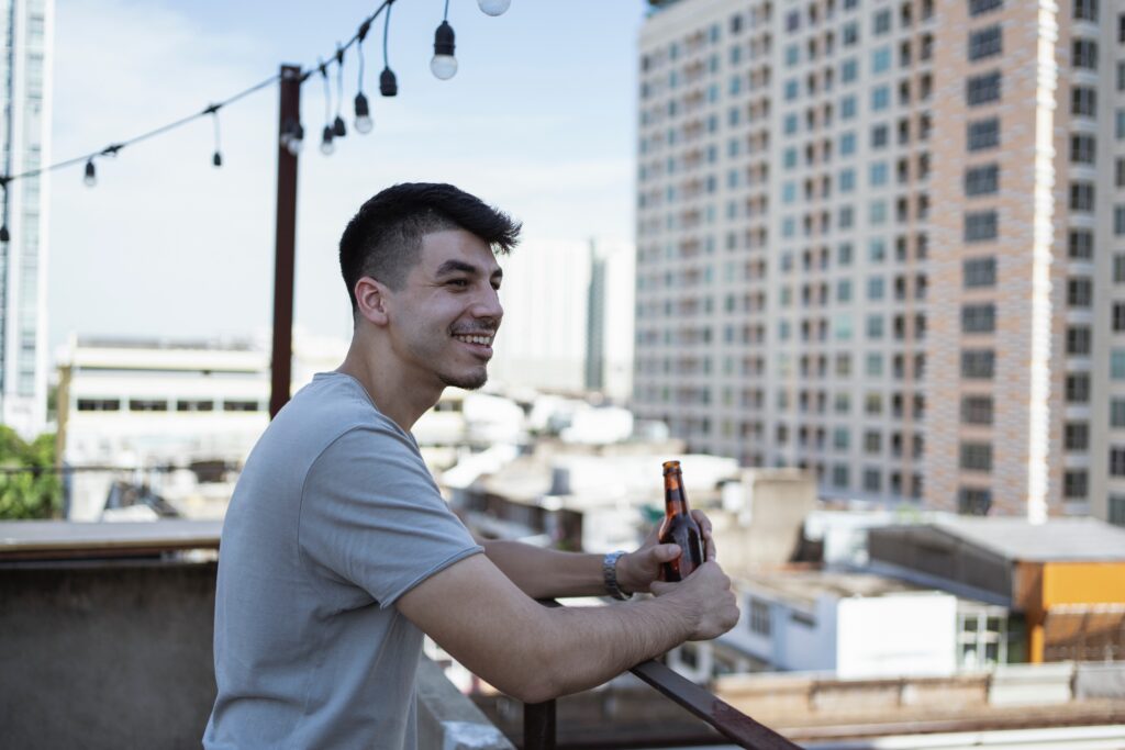 A person on a balcony smiling, holding a bottle of beer