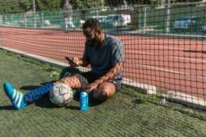 A man checks his phone while taking a break from a football match
