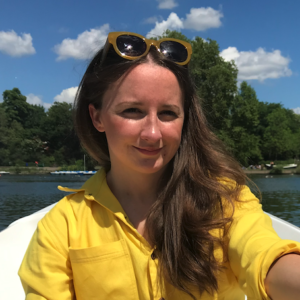 NCMH Research Champion Elin who has brown hair and is wearing a yellow jumpsuit while rowing a boat and smiling at the camera