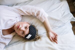 A woman lying on a bed with a sleep mask on her forehead